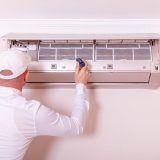 Technician in white uniform servicing a wall-mounted fan coil unit inside a UAE apartment