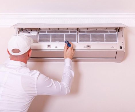 Technician in white uniform servicing a wall-mounted fan coil unit inside a UAE apartment