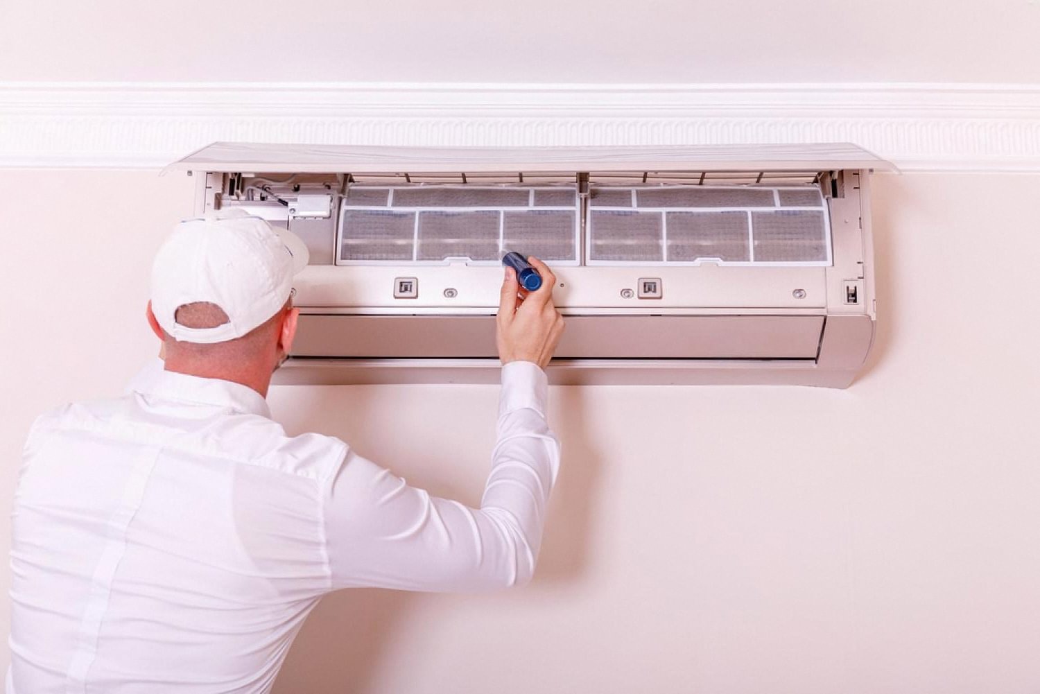Technician in white uniform servicing a wall-mounted fan coil unit inside a UAE apartment