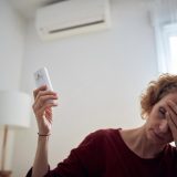 Woman holding an AC remote next to a wall-mounted air conditioner in a Dubai apartment