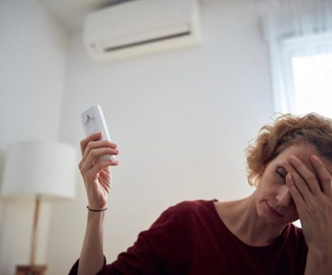 Woman holding an AC remote next to a wall-mounted air conditioner in a Dubai apartment