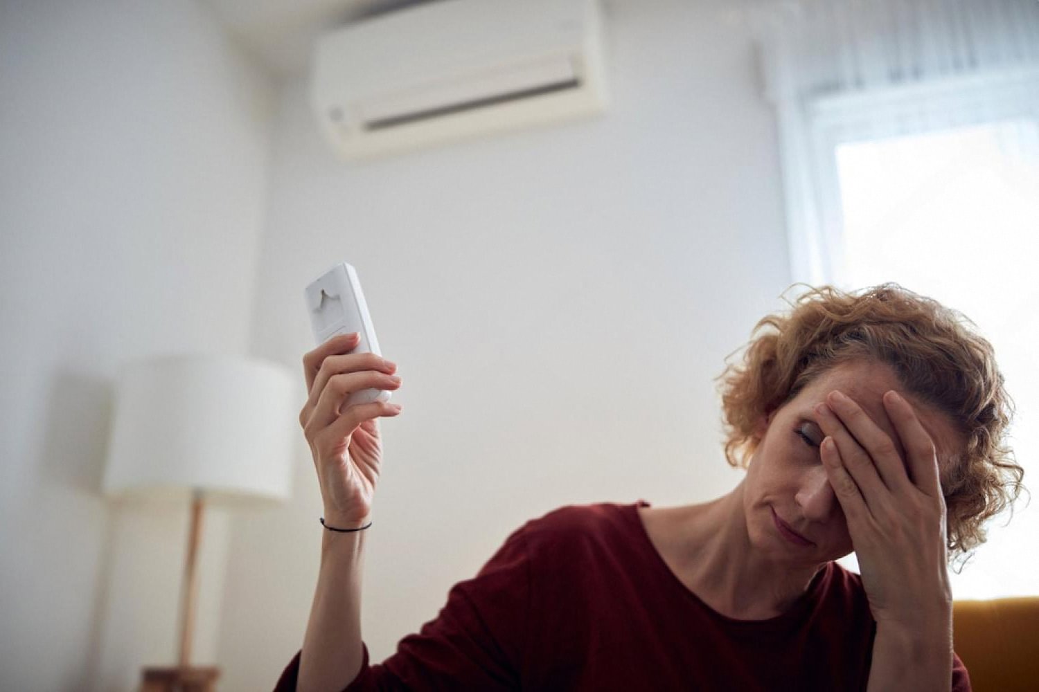 Woman holding an AC remote next to a wall-mounted air conditioner in a Dubai apartment