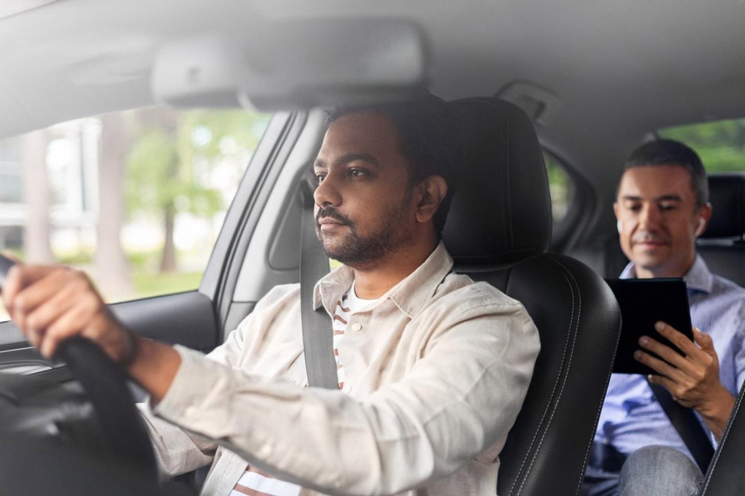 Private chauffeur driving a client through Dubai while the passenger works on a tablet in the back seat